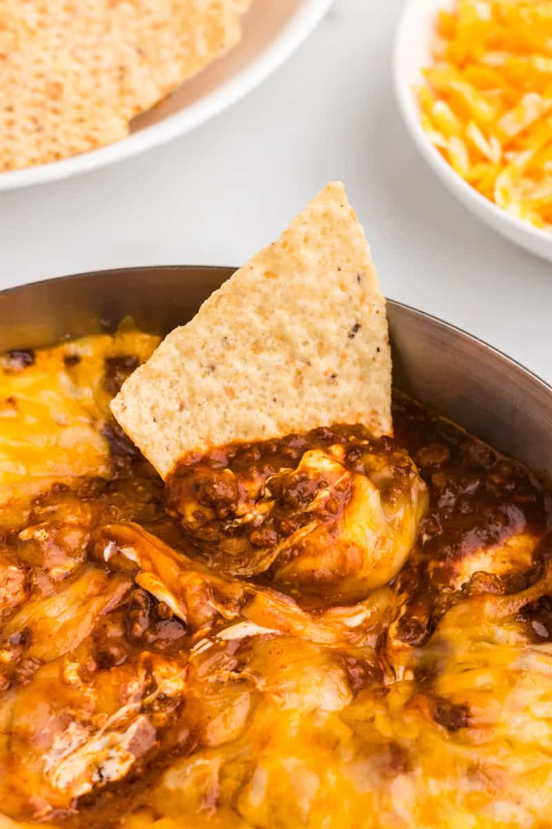 dipping a tortilla chip into the Chili Cheese Dip.