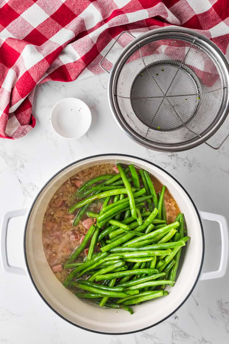 adding the green beans to the pot with the sausage.