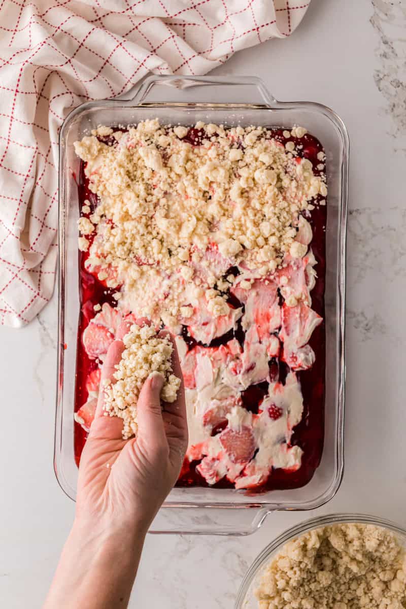 spreading the crumble topping on top of the strawberries and cheesecake filling.