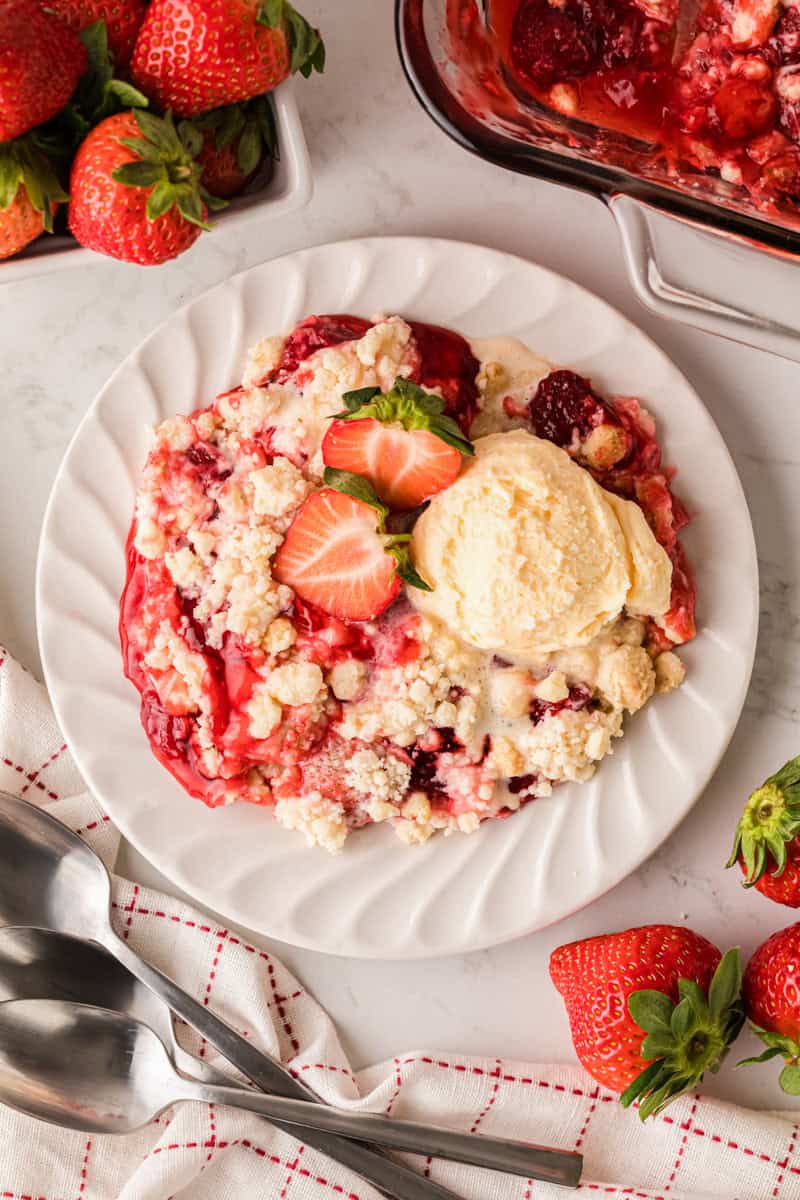 serving the Strawberry Cheesecake Dump Cake on a white plate with ice cream.