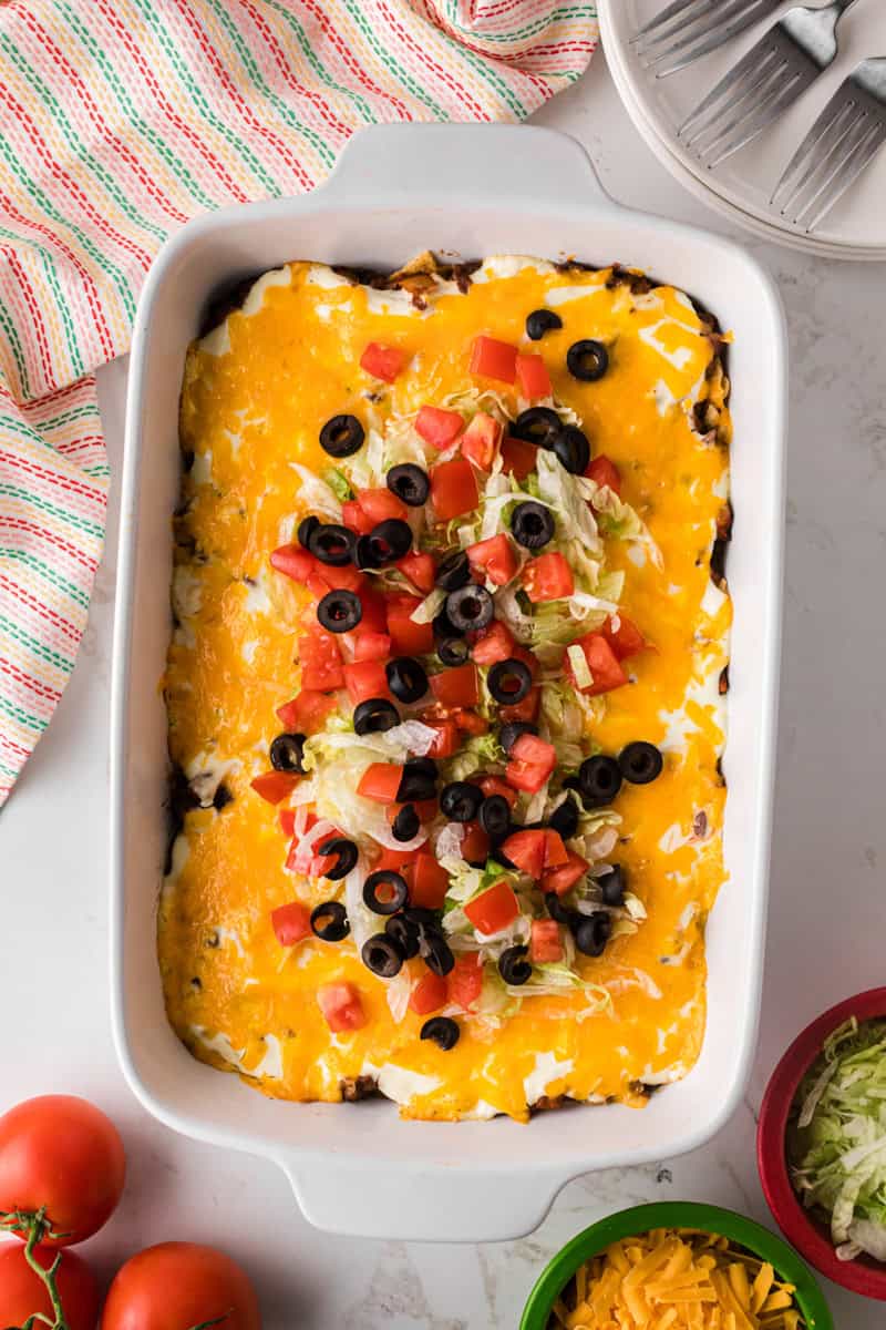 topping the taco casserole with lettuce, tomatoes and olives.