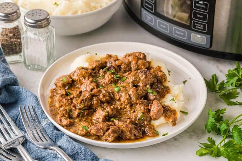 Slow Cooker Beef Tips served on a bed of mashed potatoes.