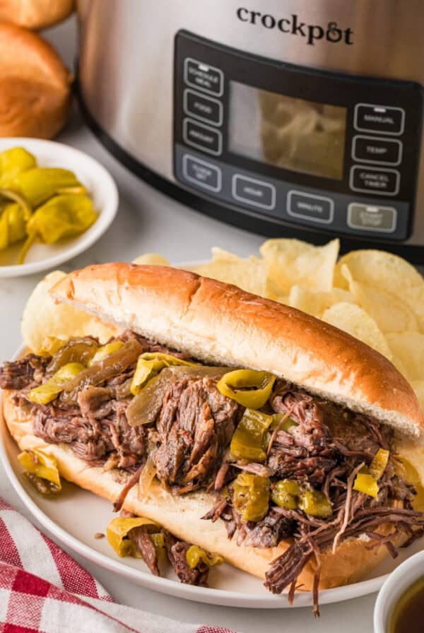 Delicious slow cooker Italian beef sandwich with tender shredded beef and peppers on a fresh bun. Pe.