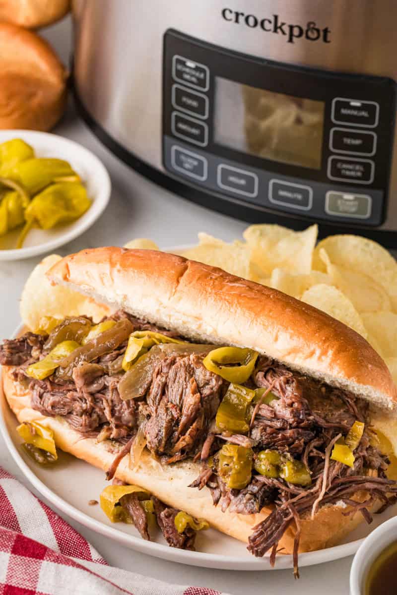 Delicious slow cooker Italian beef sandwich with tender shredded beef and peppers on a fresh bun. Pe.