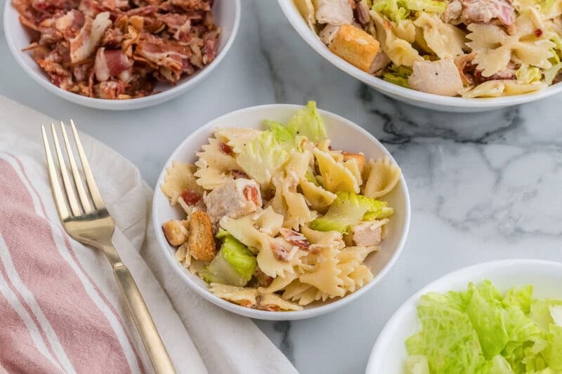 serving the Chicken Ceasar Pasta Salad in a white bowl.