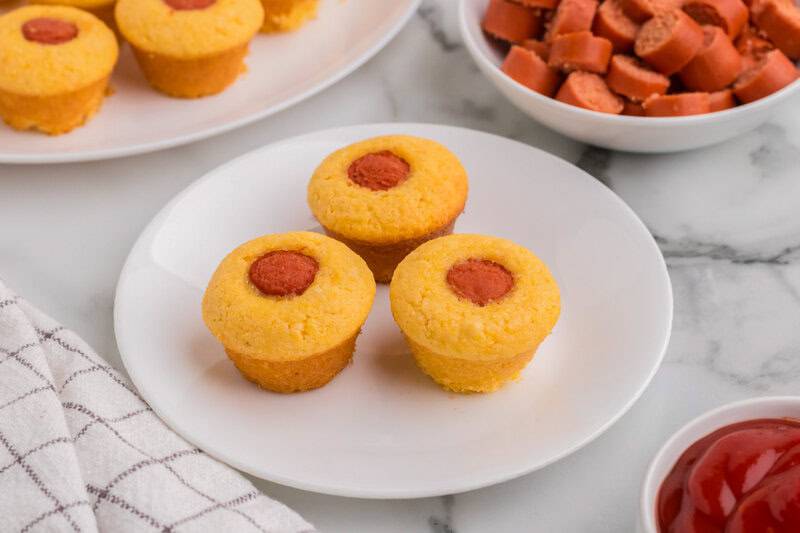 three Muffin Tin Corn Dogs served on a white plate.