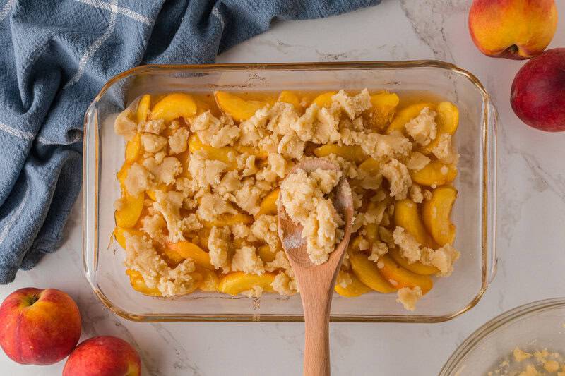 scooping the crumble topping on top of the peach cobbler.