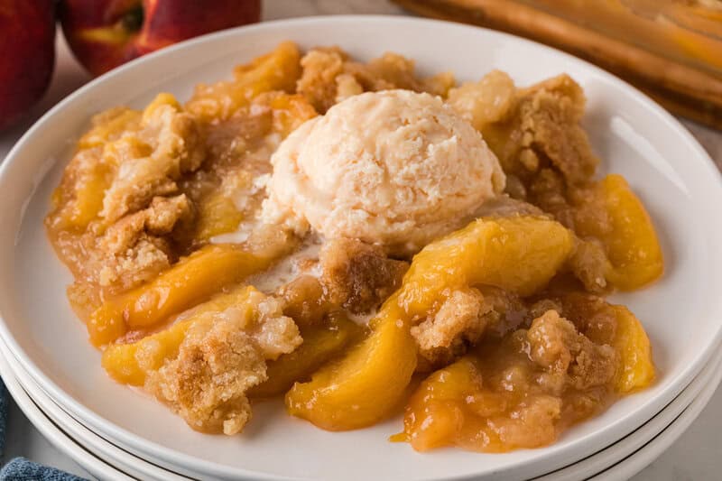 closeup of the Peach Cobbler topped with ice cream served on a white plate.