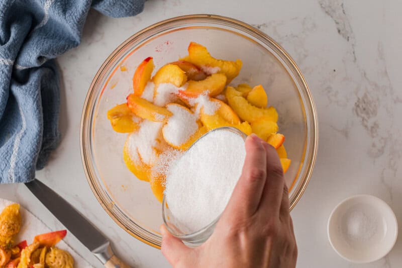 pouring sugar on top of the peaches.