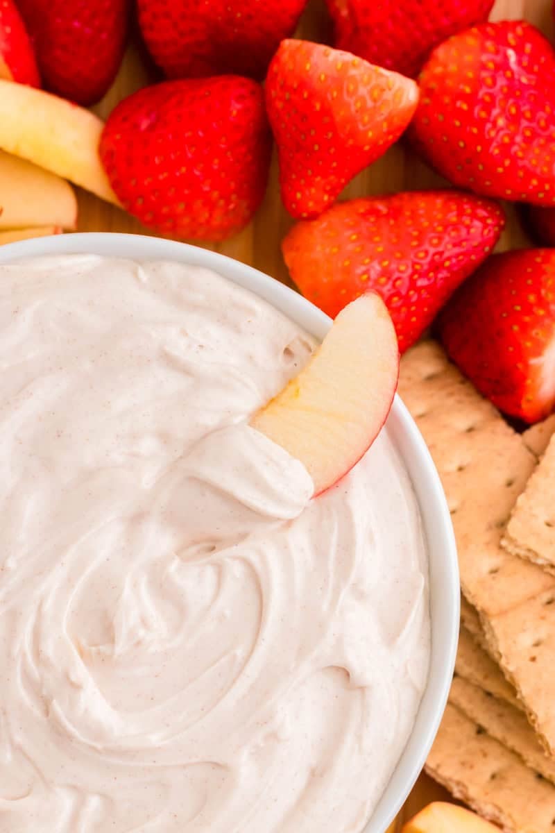 closeup of dipping an apple slice in the Snickerdoodle Dip.