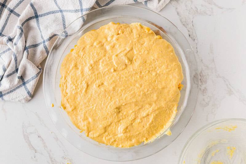 adding the cornbread mixture to the top of the taco meat.