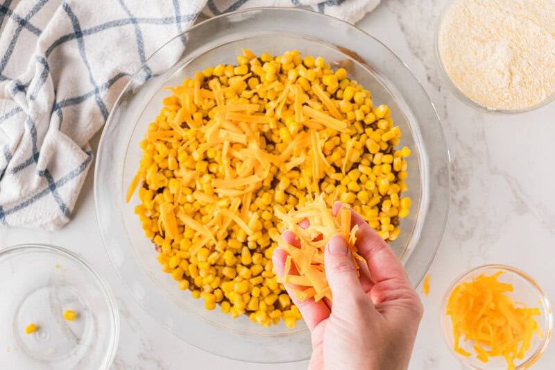 topping the taco meat with corn and cheese.