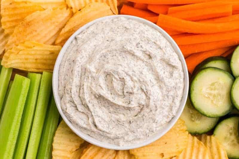 Fresh homemade dill dip in a bowl surrounded by chips and veggies.