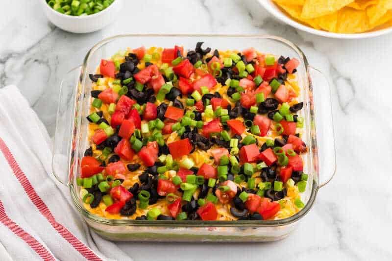 Five layer dip in a clear dish with chips for a BBQ side dish.