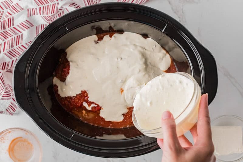 pouring the queso over the chicken in the slow cooker.