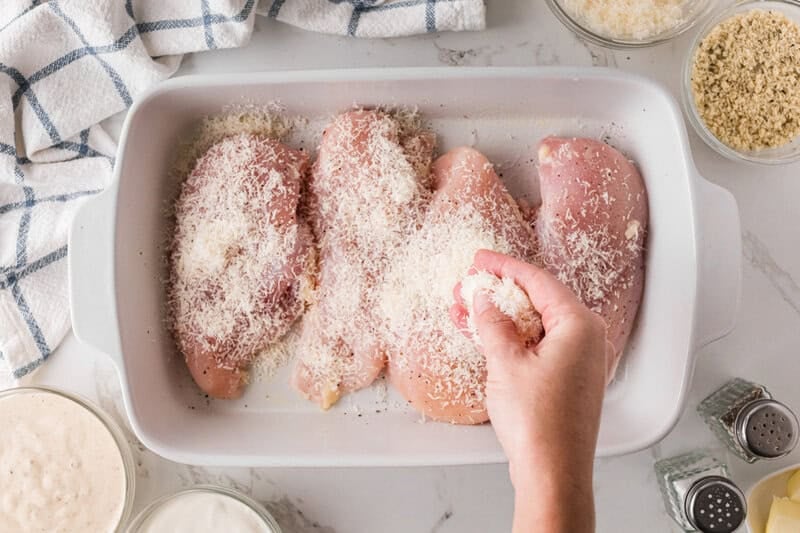 sprinkling the seasoning and Parmesan cheese over the raw chicken breasts.
