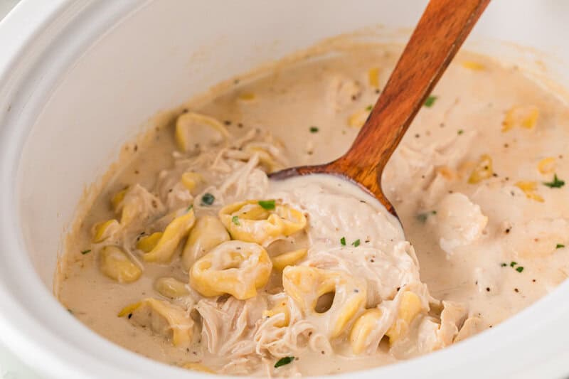 stirring the Chicken Alfredo Tortellini in the slow cooker.