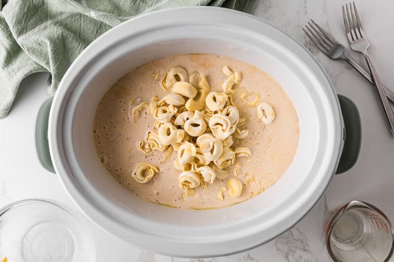adding the tortellini to the slow cooker on top of the chicken.