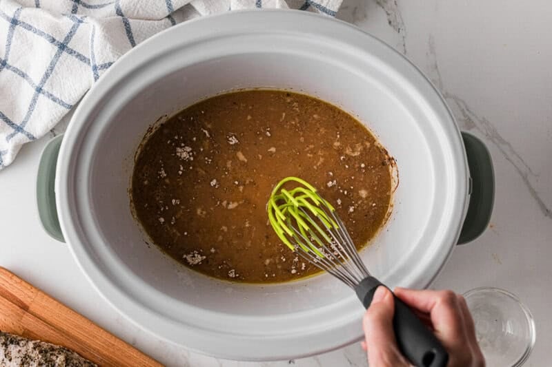 mixing together the gravy in the bottom of the slow cooker.
