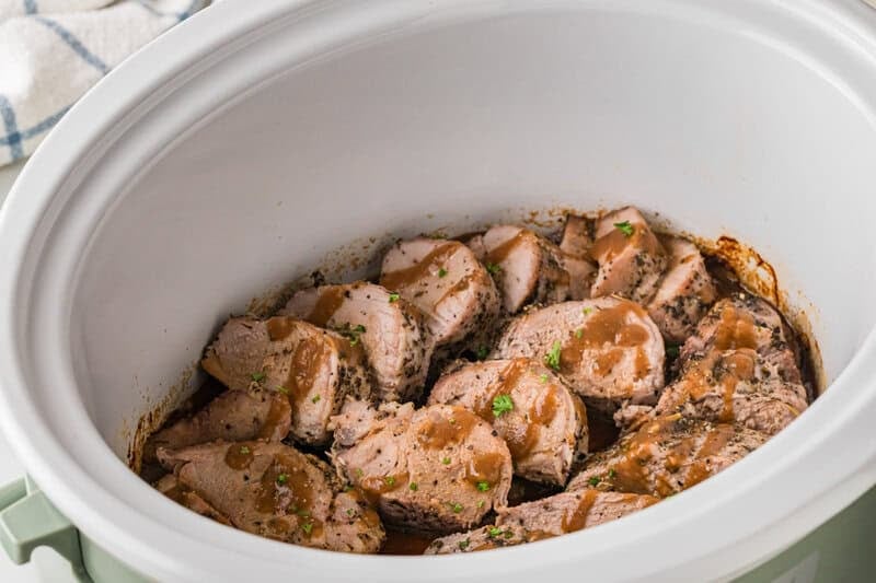 pork loin sliced in the slow cooker with gravy on it.