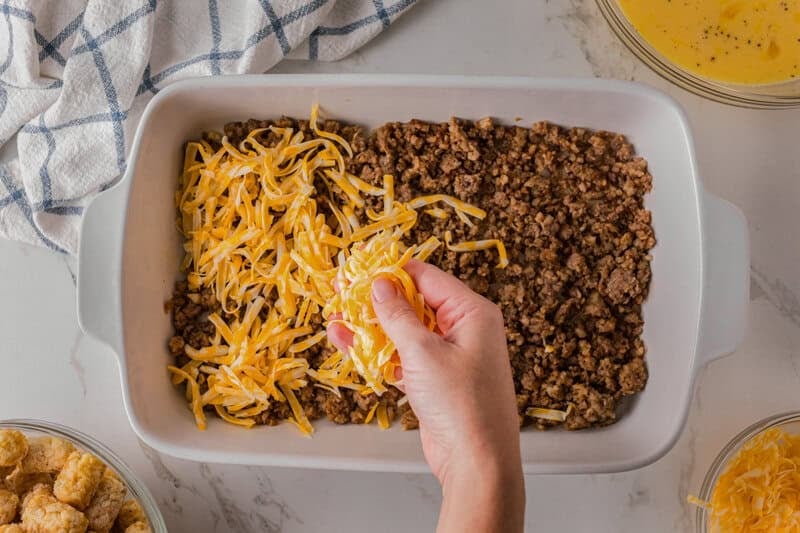 spreading the shredded cheese on top of the ground sausage.
