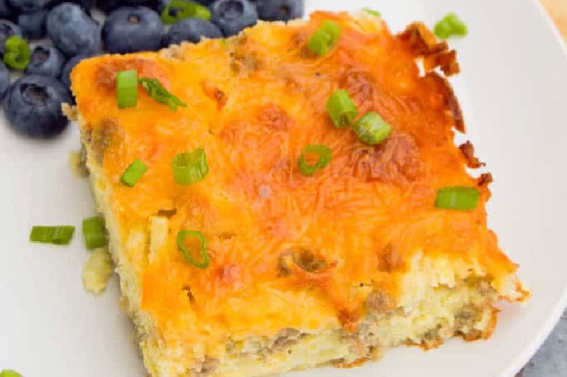 slice of the Sausage Hash Brown Breakfast Casserole served on a white plate with blueberries.