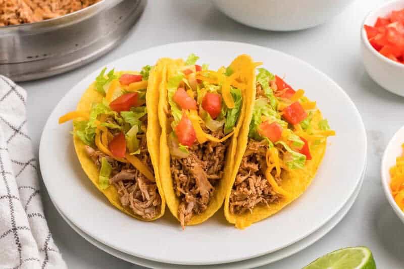 three rotisserie chicken tacos served on a white plate.