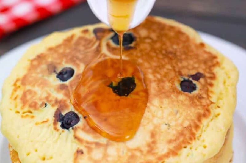 stack of Blueberry Pancakes with syrup being poured over them.