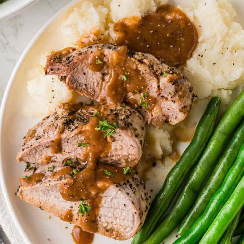 pork loin served on a white plate with mashed potatoes and green beans.