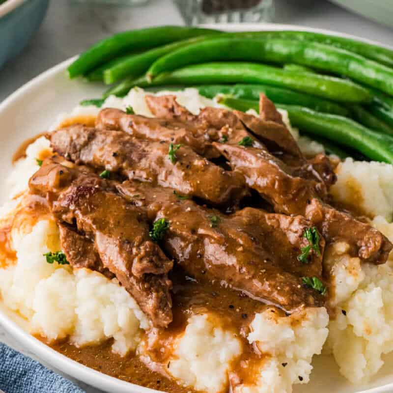 Slow Cooker Steak and Gravy served over a bed of mashed potatoes.