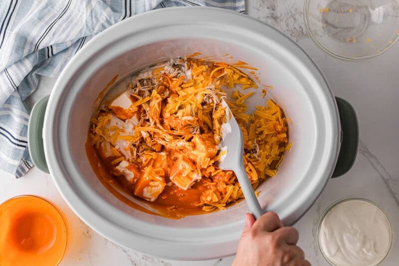 mixing together the ingredients for the dip inside the slow cooker.