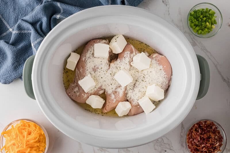top-down view of the chicken breasts, ranch seasoning and cream cheese in the slow cooker.