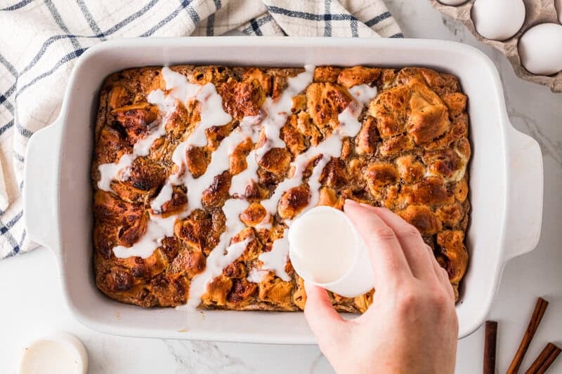 drizzling the icing over the baked cinnamon roll casserole.